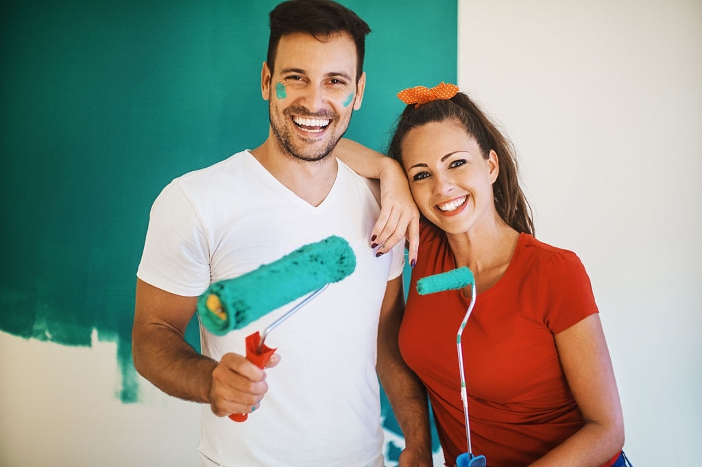 Smiling couple with paint rollers before a green wall. 