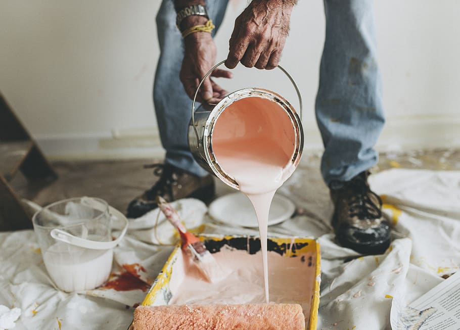 A man pouring peach colored paint in the paint bucket.