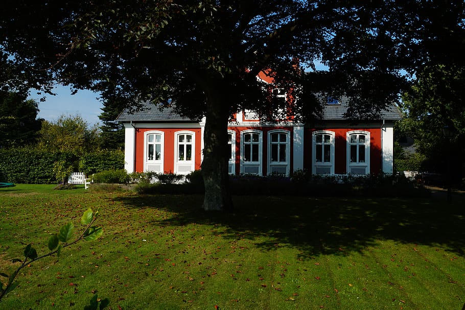 A white red colored farmhouse with a huge tree in the garden