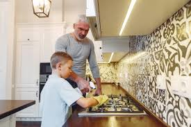 Father and son cleaning a stovetop in kitchen with a cleaner 